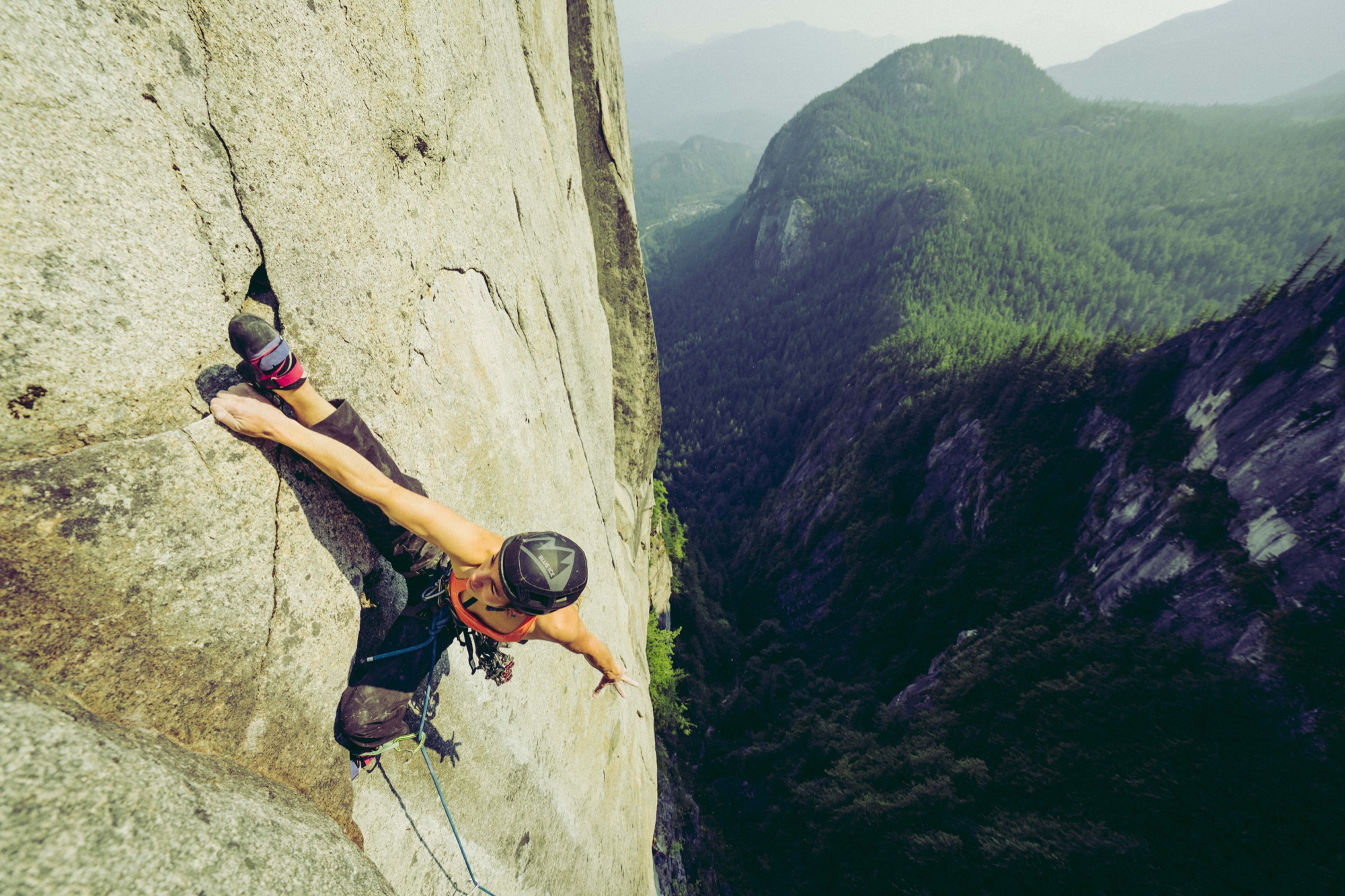 Climber ascending a granite wall above a forested mountain valley